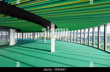 Intérieur de bureau spacieux et moderne avec façade en verre incurvé, tapis vert et lattes de plafond, colonnes et vue panoramique sur la ville, idéal pour le spa de travail d'entreprise Banque D'Images