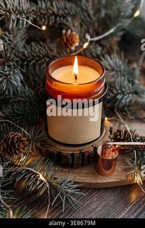 Une scène confortable avec une bougie de cire de soja allumée dans un bocal en verre brun, entouré de branches de pin et de lumières chaudes, parfait pour Noël et nouvel an cel Banque D'Images