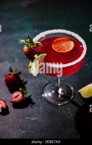 Cocktail de margarita aux fraises vibrant dans un verre avec un bord salé, garni de tranches de citron vert frais et de fraises. Une boisson estivale rafraîchissante parfaite Banque D'Images