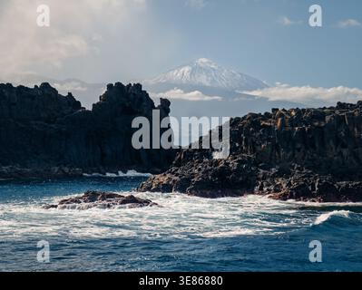 Falaises volcaniques spectaculaires et roches noires sur la côte nord de Tenerife, avec des vagues de l'Atlantique et le mont Teide s'élevant au loin près d'El pris, Cana Banque D'Images