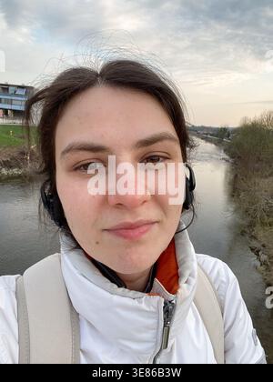 Jeune femme avec casque prenant selfie sur le pont au-dessus de la rivière. Banque D'Images