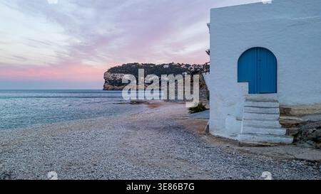 Vue pittoresque d'une maison de pêcheur blanche traditionnelle avec une porte voûtée bleue et des marches en pierre sur la plage de galets de Cala del Portixol à Javea. I Banque D'Images