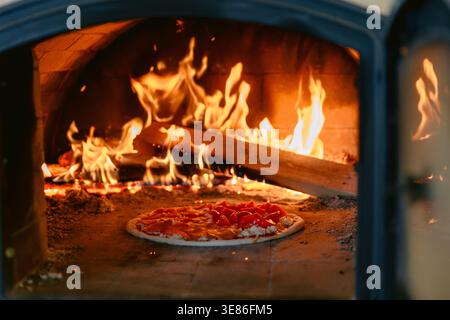 Pizza fraîche au four à bois traditionnel avec des flammes vives et des braises incandescentes. Banque D'Images