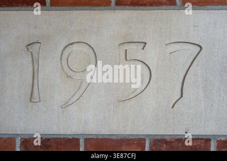 Une photo détaillée montre le numéro '1957' sculpté dans un bloc de pierre de couleur claire. Pierre angulaire du bâtiment, le long d'un mur de briques rouges. Banque D'Images