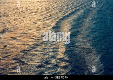 Gros plan des vagues de l'océan douces avec la lumière dorée du soleil reflétant sur la surface ondulée de l'eau. Banque D'Images