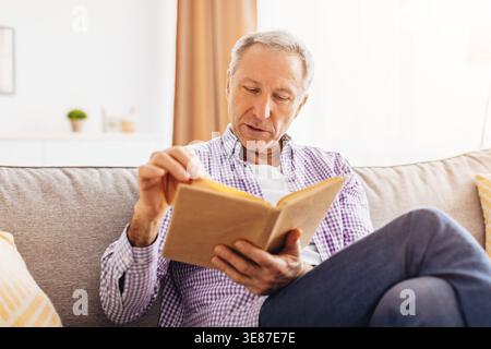 L'homme senior lit Livre sur le canapé pendant l'après-midi dans le salon confortable Banque D'Images