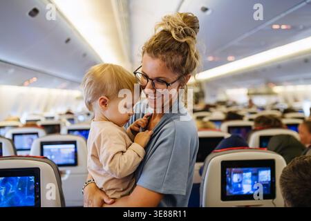 Maman calmant l'enfant bouleversé pendant le vol familial en voyageant dans l'avion. Banque D'Images