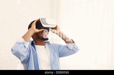 Homme noir joyeux utilisant un casque VR à la maison Banque D'Images