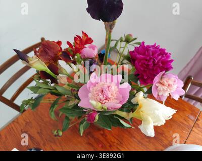 Arrangement floral simple avec pivoines et Iris. Bouquet de fleurs dans le vase à la maison sur la vue de dessus de table. Banque D'Images