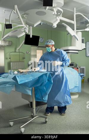 Cliché vertical d'un chirurgien d'âge moyen préparant des instruments à côté du patient dans la salle d'opération, pour faciliter le déroulement des opérations chirurgicales et les soins stériles. Idéal pour la santé, l'hôpital, le marketing de traitement Banque D'Images