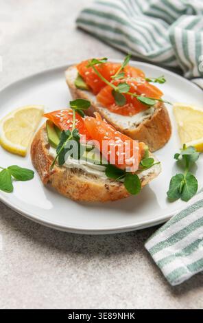 Deux mini-sandwichs sains avec saumon fumé, avocat, fromage à la crème et pousses de pois dans une assiette Banque D'Images