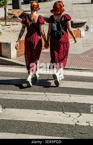 Jeunes femmes jumelles soeurs avec les cheveux roux dans des robes assorties marchant dans la rue ensemble Banque D'Images