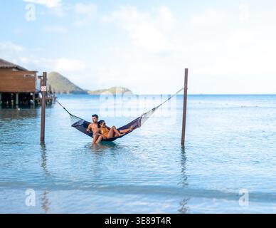 Un couple profite d'un après-midi serein se prélasser ensemble dans un hamac au-dessus des eaux calmes. Un couple multiethnique diversifié d'une femme asiatique et d'un homme caucasien en vacances de luxe Banque D'Images