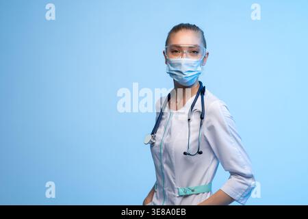 Médecin féminin portant un masque facial et des lunettes, debout avec confiance, fournissant des soins médicaux et une protection dans les soins de santé Banque D'Images