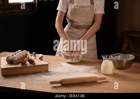 Boulanger pétrissant la pâte dans un bol en verre pour le pain fait maison sur le comptoir de cuisine en bois farineux dans un cadre rustique Banque D'Images