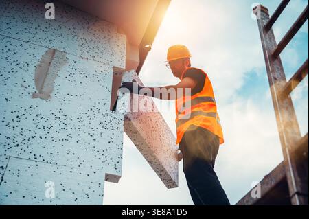 Le travailleur installe du matériau de construction sur le chantier pendant la journée près de l'échafaudage en plein soleil Banque D'Images