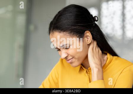 Femme debout souffrant de douleurs sévères au cou, massant ses muscles tendus en raison de l'inconfort, du stress, de la raideur et de l'épuisement, indiquant un problème de santé Banque D'Images