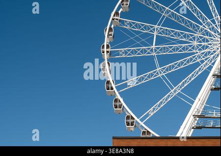 Sous un ciel bleu éclatant, une grande roue domine la ville, invitant les amateurs de sensations fortes à profiter de vues panoramiques et de sensations fortes lors de la balade Banque D'Images