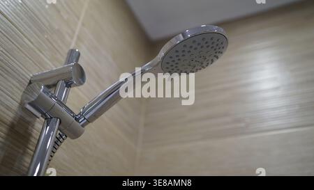 Gros plan à angle bas du luminaire de pomme de douche chromé moderne. Le mur carrelé beige neutre crée un arrière-plan propre. Concept d'hygiène, routine quotidienne, plumbin Banque D'Images