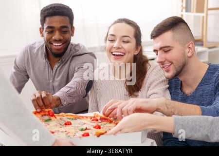 Happy friends eating pizza, avoir home party Banque D'Images