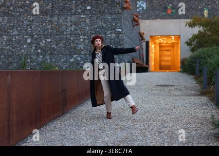 Femme élégante marchant dans l'espace urbain au crépuscule, tenue moderne et style de vie confiant dans l'environnement de la ville. Banque D'Images