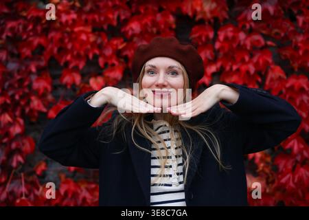 Femme souriante avec des feuilles d'automne rouges, des couleurs d'automne vibrantes et un portrait de style de vie urbain élégant. Banque D'Images