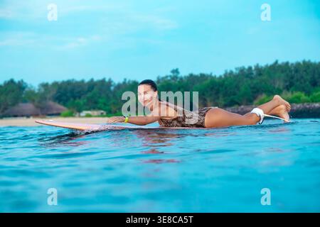 Jeune femme riant tout en pagayant à bord sur l'eau turquoise calme, ambiance ludique et retraite détendue Banque D'Images
