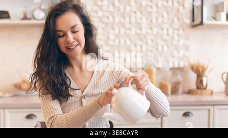 Jeune femme prépare le thé dans une cuisine confortable pendant l'après-midi Banque D'Images