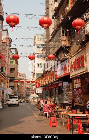 Des lanternes rouges sont suspendues au-dessus d'une rue animée bordée de restaurants et de boutiques dans un Ganzhou, en Chine, où les habitants dînent à des tables en plein air Banque D'Images