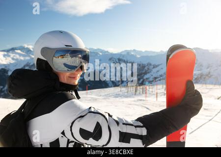 Femme skieuse tient des regards de ski rouges avec des lunettes réfléchissantes montrant la station enneigée. Lumière du soleil les montagnes alpines, le paysage d'hiver créent une ambiance énergique Banque D'Images