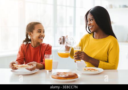 Petit déjeuner familial avec mère et fille appréciant jus et nourriture à la maison pendant la matinée Banque D'Images