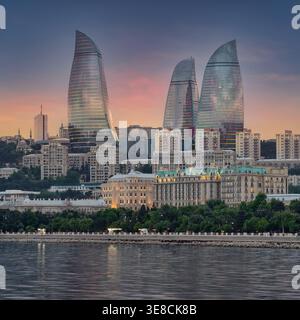 Emblématiques Flame Towers et la ligne d'horizon de la ville de Bakou illuminées au coucher du soleil, avec la mer Caspienne et le boulevard Bakou au premier plan, Bakou, Azerbaïdjan Banque D'Images
