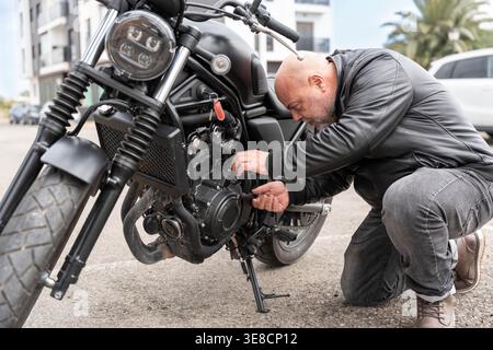Mécanicien agenouillé à côté de la moto, inspectant et ajustant le moteur extérieur.détail axé sur les travaux de réparation et d'entretien sur la rue Banque D'Images