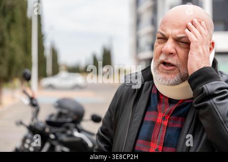Homme tenant sa tête dans la douleur après un accident de moto avec une attelle cervicale Banque D'Images