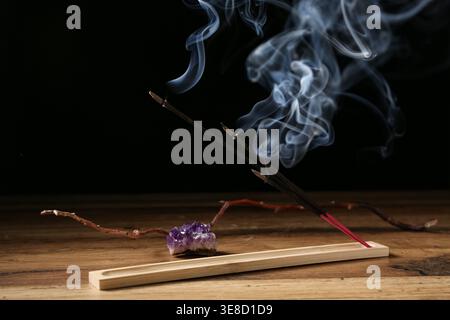 Support avec bâtons d'encens fumants sur une table en bois sombre Banque D'Images
