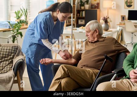 Homme caucasien senior recevant un traitement médical par une infirmière jeune adulte, surveillant l'accès IV et la guérison. Utile pour les soins aux aînés, les services infirmiers, le marketing de la vie assistée Banque D'Images