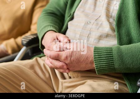 Gros plan d'un homme caucasien âgé handicapé reposant les mains serrées dans un fauteuil roulant, représentant les soins aux aînés et le soutien à la mobilité. Utile pour les soins de santé, la prestation de soins, le marketing de réadaptation Banque D'Images