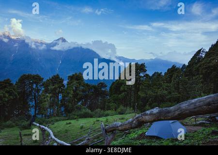Cette image capture un paysage de montagne tranquille avec une tente dressée dans un pré verdoyant. La scène est entourée d'arbres denses et imposants Banque D'Images