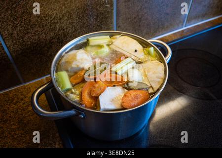 Bouillon de poulet maison avec des légumes frais mijotant dans une grande casserole en acier inoxydable sur une cuisinière à induction. Haut en bas, vue rapprochée, pas de gens Banque D'Images