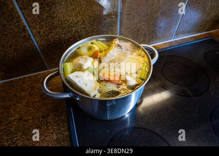 Bouillon de poulet maison avec des légumes frais mijotant dans une grande casserole en acier inoxydable sur une cuisinière à induction. Haut en bas, vue rapprochée, pas de gens Banque D'Images