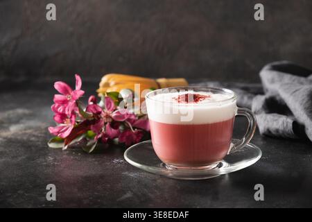Latte matcha rose avec fleurs de sakura décorées en poudre sur fond noir foncé. Boisson tendance. Sans caféine. Gros plan. Banque D'Images
