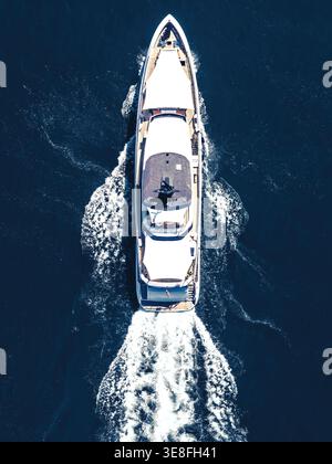 Vue aérienne d'un yacht blanc de luxe naviguant dans l'eau bleu profond laissant un sillage blanc. Banque D'Images