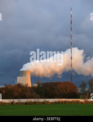 Vapeur de la centrale électrique Rostock montant à côté du mât haut et des câbles contre un ciel nuageux sombre au-dessus de champs ouverts. Banque D'Images