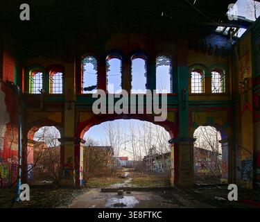 Intérieur d'usine abandonné avec graffiti de fenêtres cintrées et porte ouverte. Banque D'Images