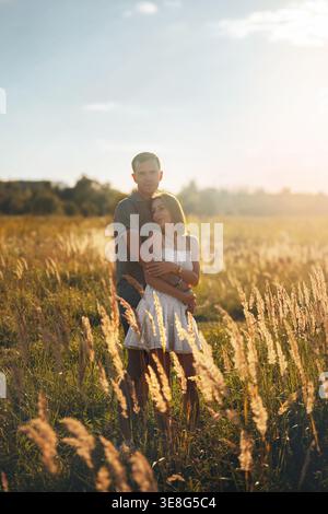 Un couple partage une étreinte intime dans un champ doré de hautes herbes pendant le coucher du soleil. La lumière chaude améliore l'atmosphère romantique comme ils connectent l'esprit Banque D'Images
