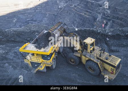 Vue aérienne d'une grande chargeuse sur pneus chargeant du minerai sombre dans un camion à benne basculante lourd dans une mine à ciel ouvert à Santa Lucia de Gordon, Castille-et-Léon, Banque D'Images