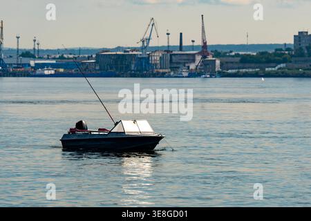Petit bateau de pêche ancré sur Calm River près du port industriel avec grue Skyline au crépuscule Banque D'Images