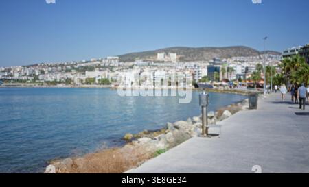 Promenade en bord de mer, scène bokeh légèrement floue avec front de mer, bâtiments urbains lointains et palmiers le long d'un chemin ; arrière-plan copyspace calme Banque D'Images