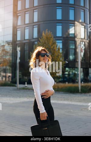 Femme debout dans la ville avec sac à main. Belle femme d'affaires portant une tenue élégante et des lunettes de soleil. Apparence professionnelle de l'entreprise. Portrait urbain Banque D'Images