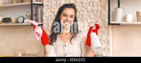 Femme nettoyage dans la cuisine tout en souriant avec des fournitures de nettoyage Banque D'Images